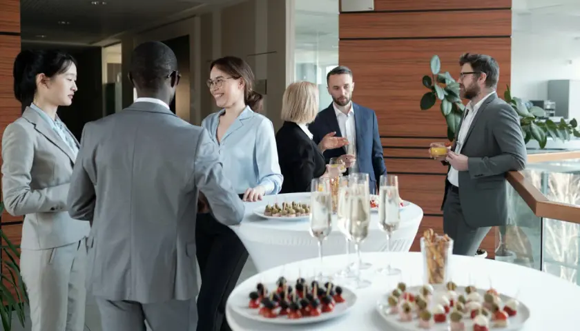 Profesionales conversan y disfrutan de canapés y bebidas en un evento corporativo.