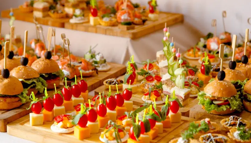 Variedad de aperitivos para bodas: mini hamburguesas, canapés de salmón, brochetas de tomate y queso, y tartas saladas. ¡Un festín visual!