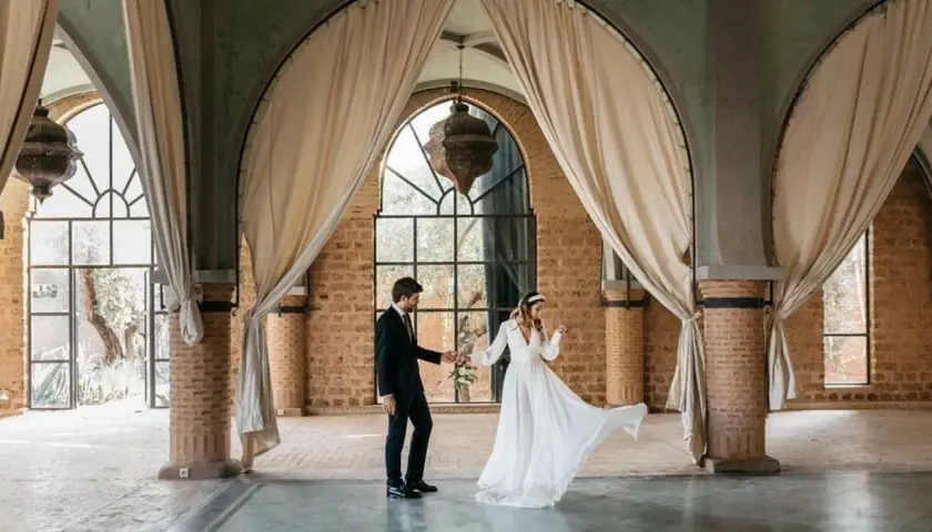 Novios bailan en un salón con arcos y cortinas, celebrando que las bodas son a los 10 años.