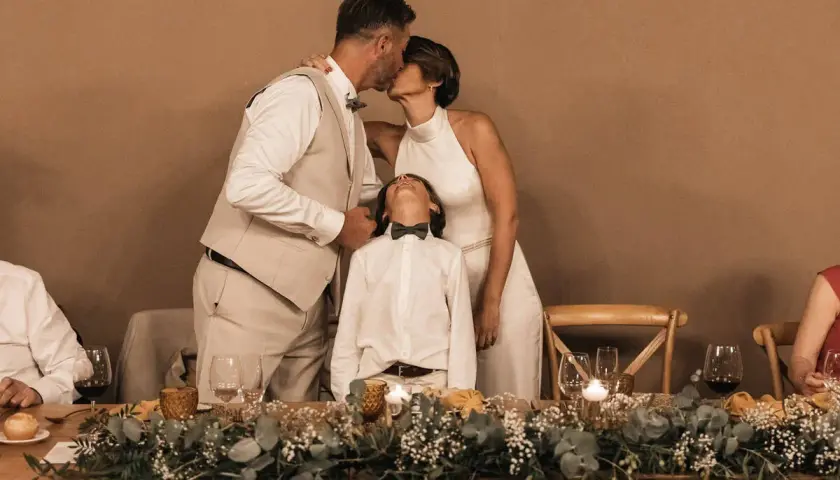 Una pareja se besa tiernamente mientras su hijo mira al cielo, celebrando bodas de plata, oro y platino.