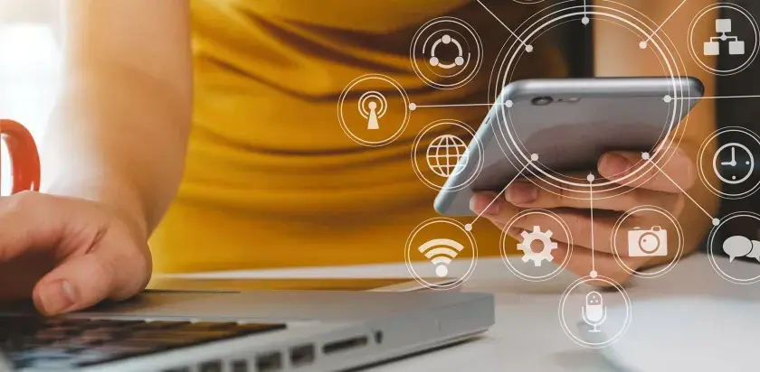 Persona usando un móvil y portátil con iconos de analítica digital superpuestos.