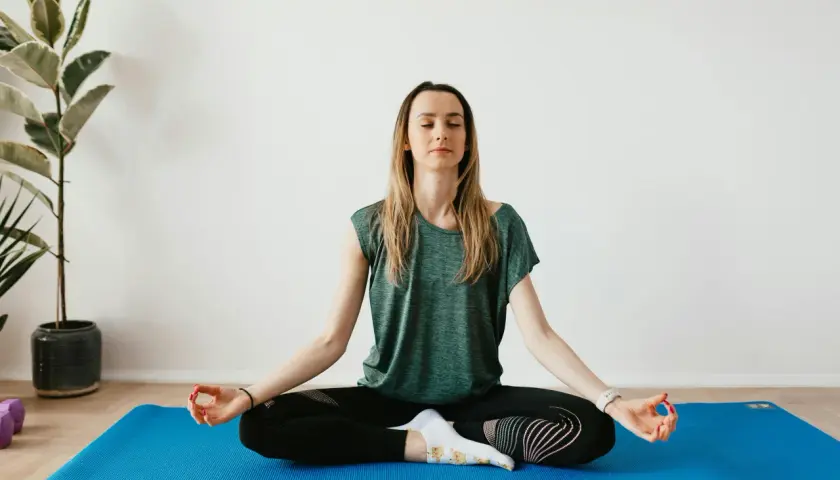 Mujer meditando en postura de loto sobre una esterilla azul. Practica 8 ejercicios de respiración para relajarse.