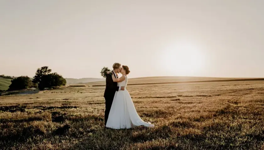 Novios besándose en un campo dorado al atardecer, un hermoso escenario para bodas en mayo.