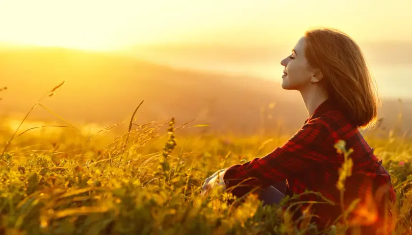 Mujer sonríe en un campo al atardecer, disfrutando de la paz y fortaleciendo su autoestima personal.