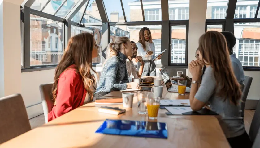 Un grupo diverso de profesionales participa en un workshop, discutiendo ideas alrededor de una mesa con laptops y bebidas.