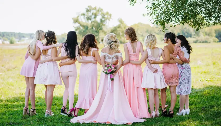 Novia rodeada por sus damas de honor, todas vestidas de rosa, en un campo verde.