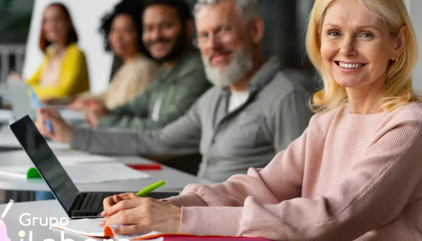 Mujeres y hombres participan en un curso formador de formadores online. Sonríen mientras aprenden en un aula moderna.