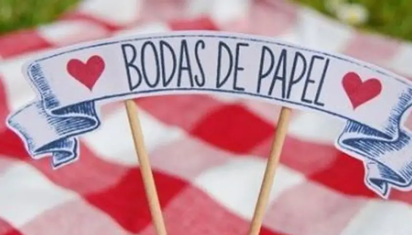 Un letrero de "Bodas de Papel" con corazones rojos, sobre un mantel de cuadros rojos y blancos.