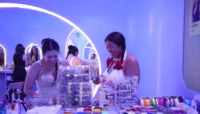 Dos mujeres sonríen en un puesto de accesorios para el cabello y cintas, parte de eventos de marca.