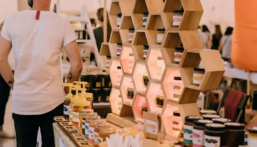 Exhibición de mieles artesanales en ferias empresariales. Tarros de miel en estanterías de madera con forma de panal, iluminados.