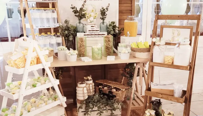 Un candy bar rústico con dulces, botellas de agua y un cartel "Mesa Dulce".