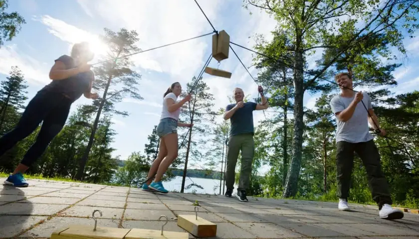 Un grupo participa en un juego de team building outdoor, tirando de cuerdas para mover un objeto de madera.