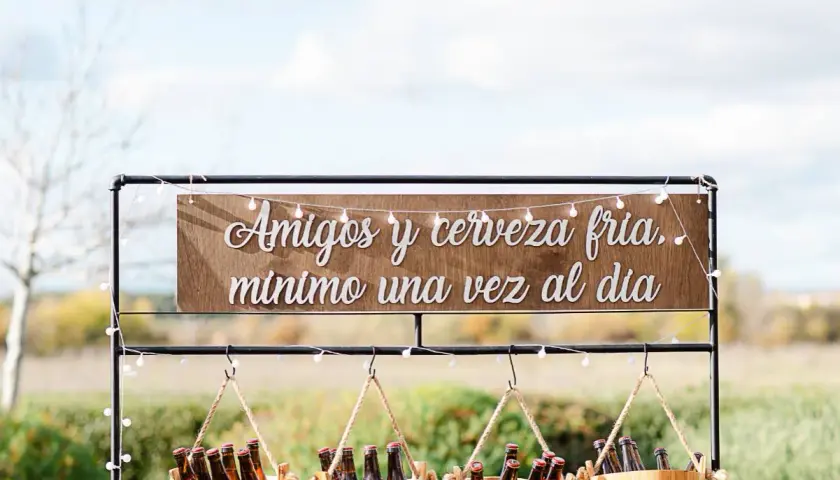 Decoración barra libre boda: letrero "Amigos y cerveza fría, mínimo una vez al día" sobre cubos de cerveza.