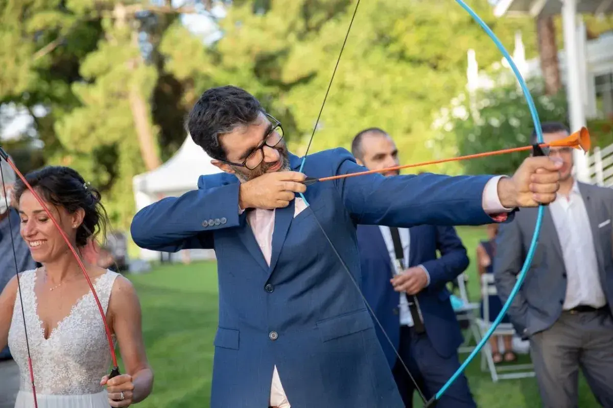 Novio con arco y flecha, parte de los juegos de bodas. La novia sonríe a su lado.