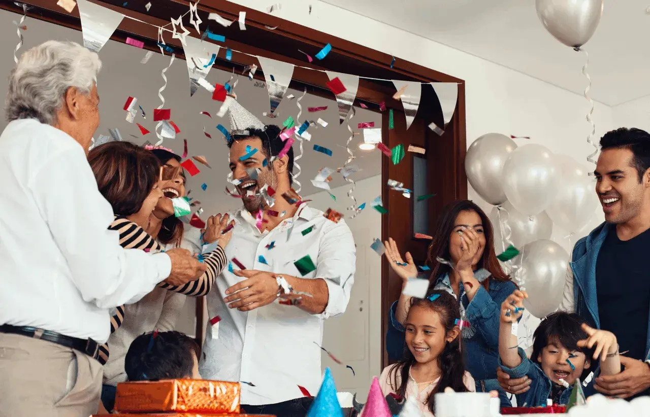 Familia celebrando fiestas sorpresa con confeti y globos. Todos ríen y se abrazan, creando un ambiente de alegría.