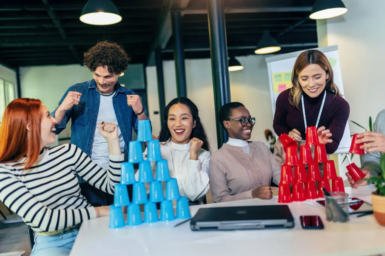 Equipo celebrando en juegos de empresa, apilando vasos de colores.