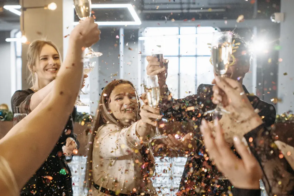 Gente celebrando un aniversario de empresas con confeti y copas de champán.