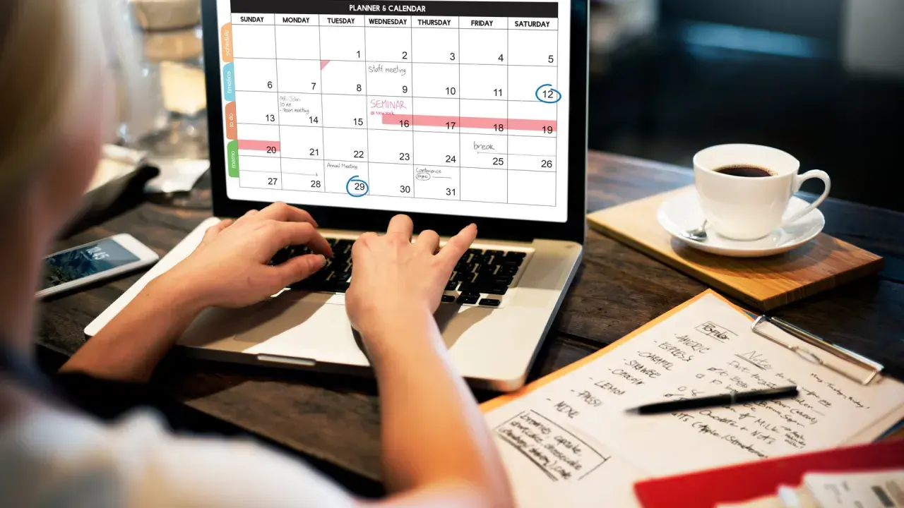 Persona organiza su **curso gestión administrativa** en un calendario digital, con una taza de café al lado.