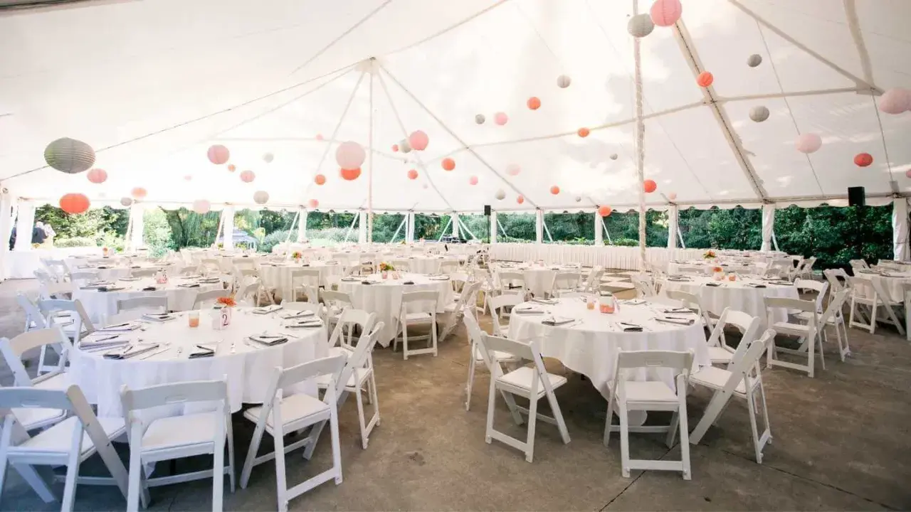Carpa blanca con mesas redondas y sillas blancas, decorada con farolillos de colores. Un espacio ideal para **sitios de eventos**.