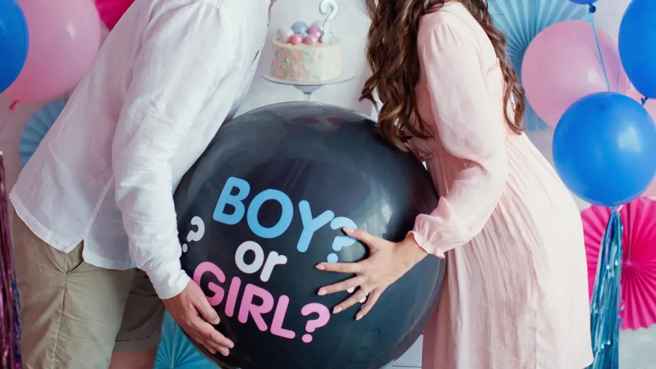 Pareja celebra un gender reveal, con un globo negro que pregunta "BOY or GIRL?".