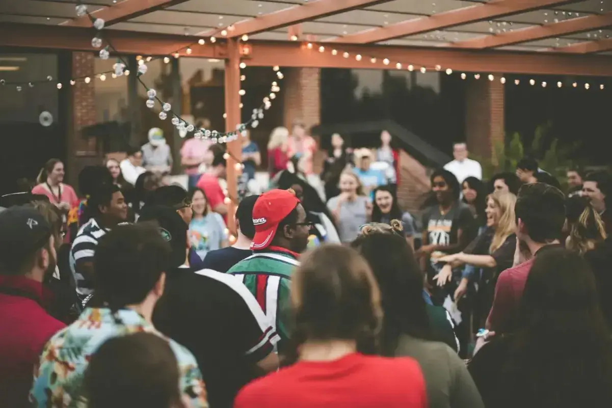 Grupo de personas disfrutando en una fiesta al aire libre, con luces decorativas. ¡Excelentes ideas para cenas de empresa!