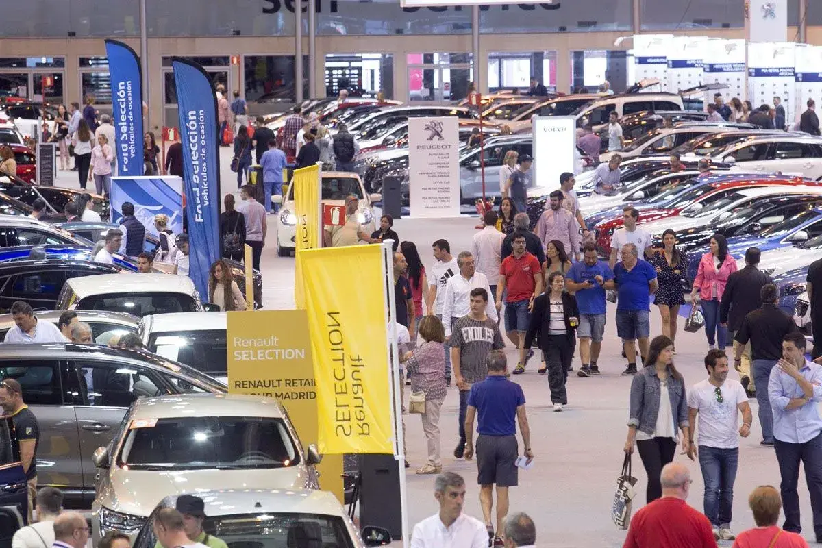 Gente paseando entre coches en una feria comercial. Banderolas de Ford y Renault anuncian vehículos de ocasión.