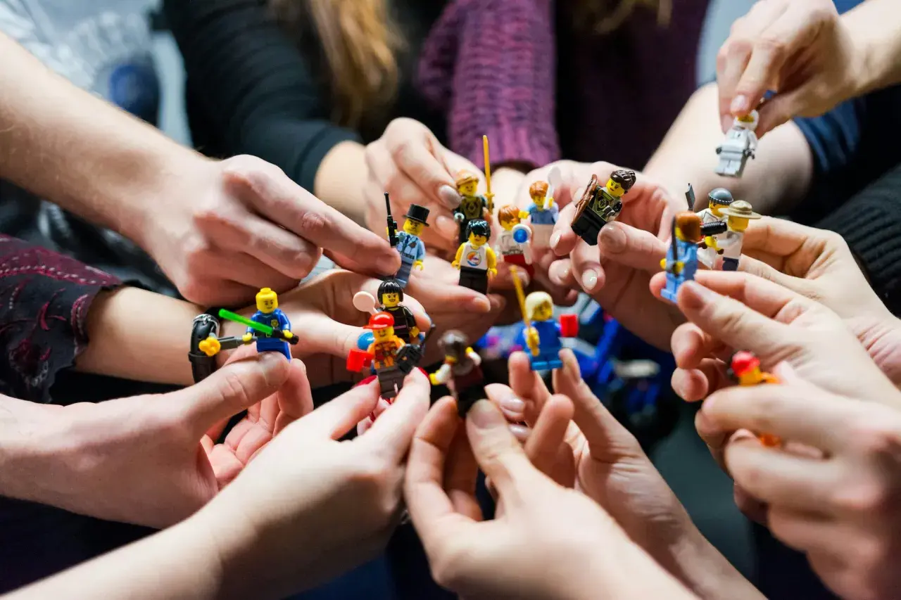 Manos sostienen figuras de Lego, creando un ambiente de **actividades team building originales** y divertidas.