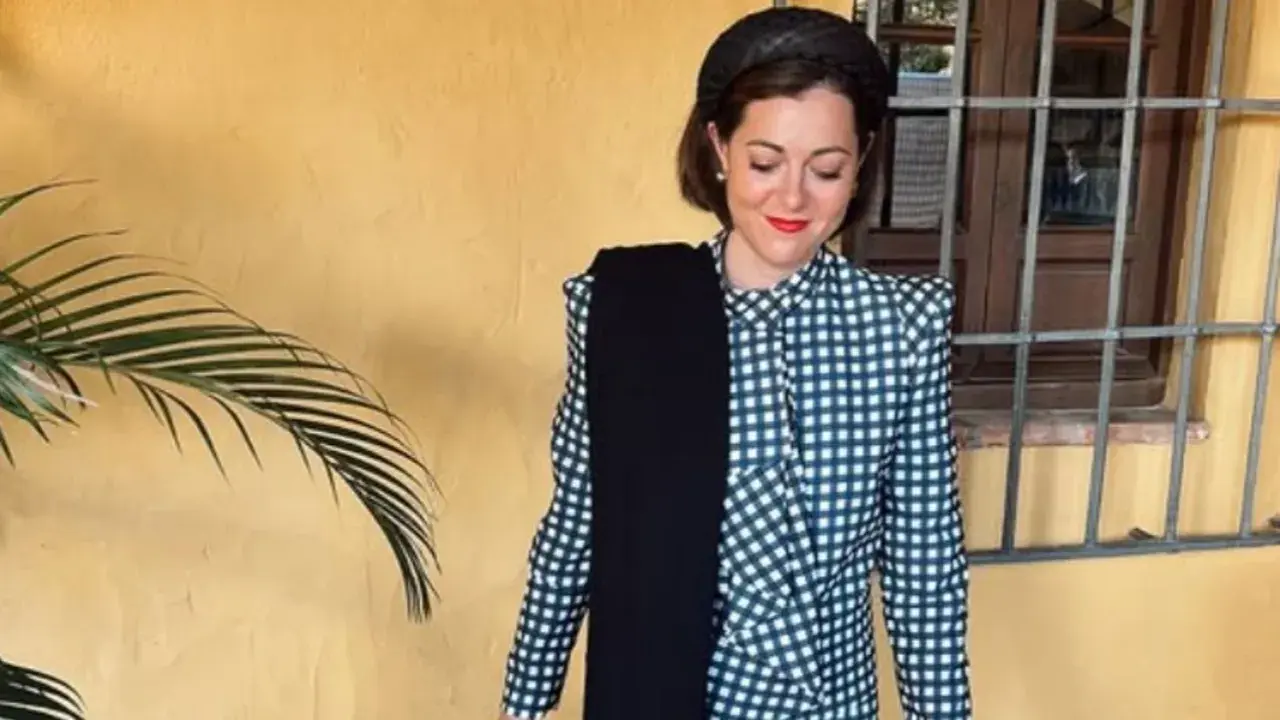 Mujer con traje de cuadros, tocado y bufanda negra. Un ejemplo de dress code elegante para un evento.