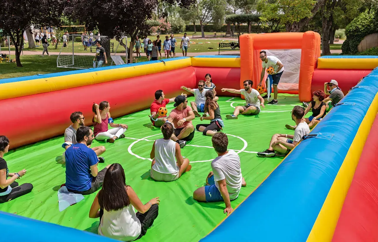 Gente disfrutando de un día familiar en empresas, sentados en un campo de fútbol inflable, riendo y jugando.
