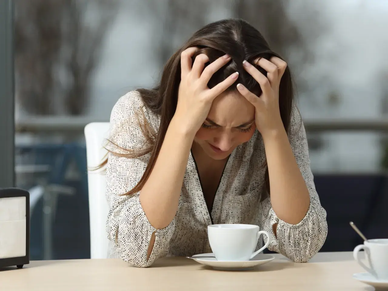 Mujer con las manos en la cabeza, mirando su taza de café, quizás porque le doy tantas vueltas a las cosas.