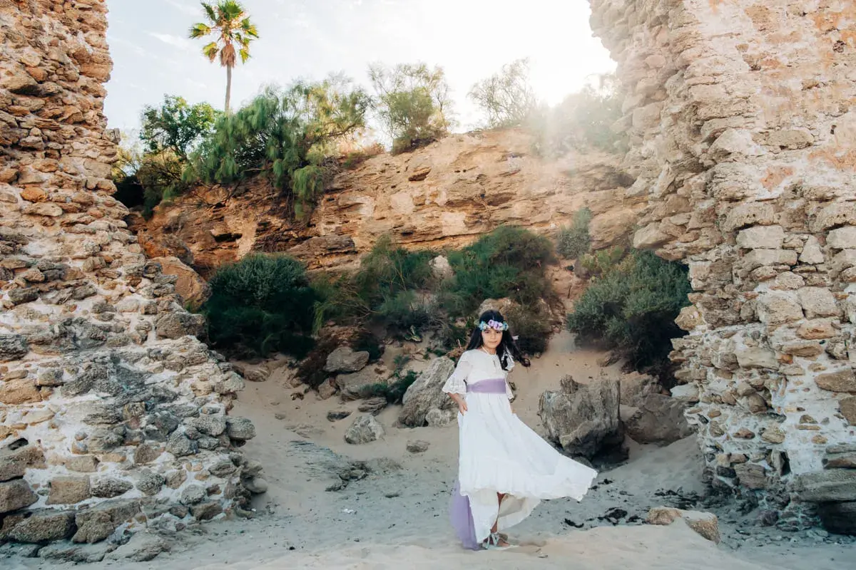 Niña con vestido blanco y corona de flores, posando en unas ruinas, un escenario perfecto para comuniones al aire libre.