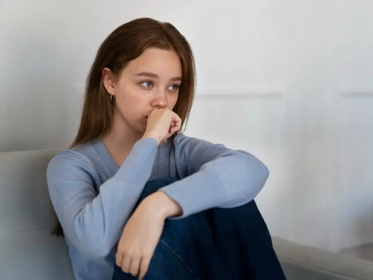 Joven con un bajón emocional, sentada en un sofá, con la mano en la boca y la mirada perdida.