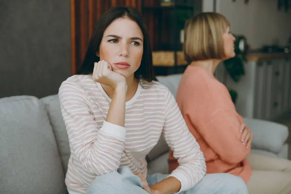 Dos mujeres sentadas en un sofá, una con expresión de aburrimiento, quizás pensando como tratar a una persona que siempre se queja.