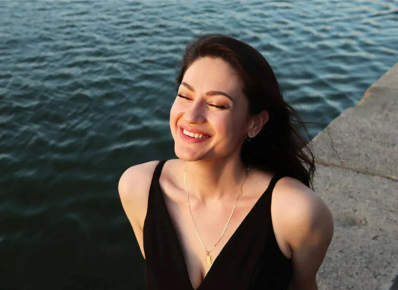 Una mujer sonríe con los ojos cerrados, sintiendo el agradecimiento por un momento de paz junto al agua.