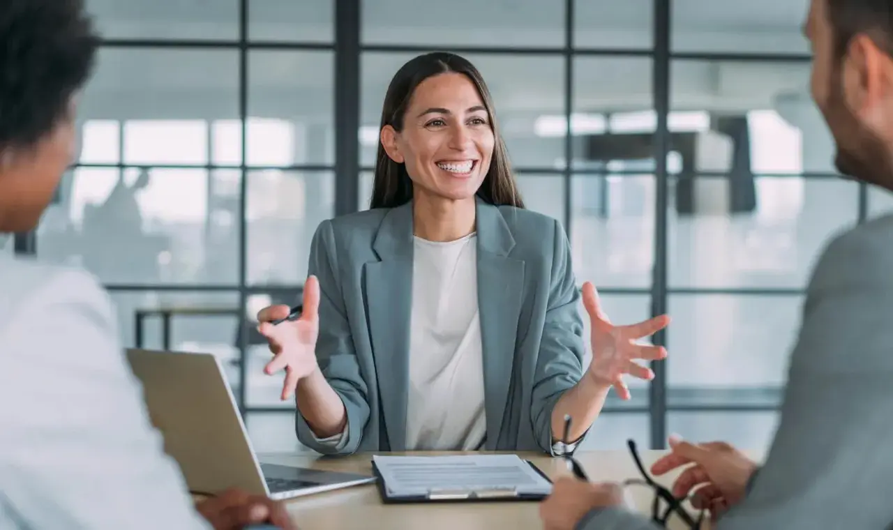 Mujer sonriente explica algo en una reunión. Podría ser un curso de mediación gratis.