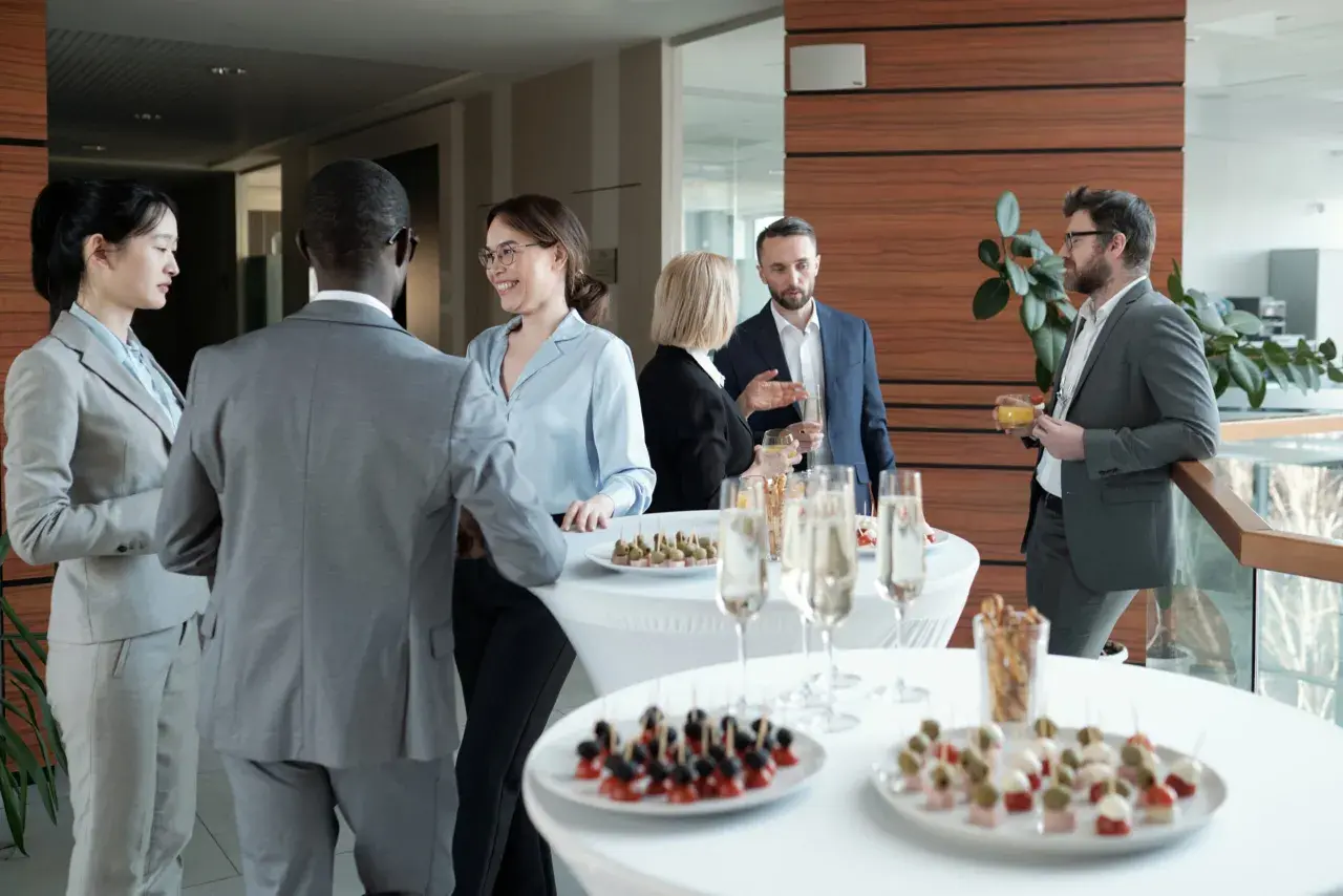 Profesionales conversan y disfrutan de canapés y bebidas en un evento corporativo.