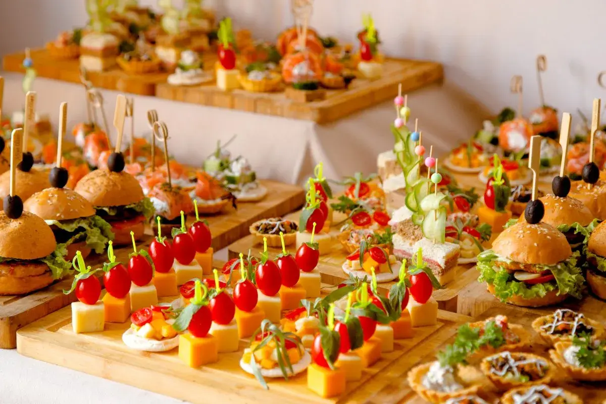 Variedad de aperitivos para bodas: mini hamburguesas, canapés de salmón, brochetas de tomate y queso, y tartas saladas. ¡Un festín visual!