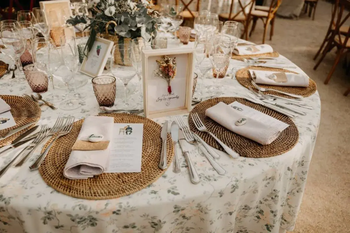 Mesa de boda con manteles florales, vajilla y centros de mesa rústicos.