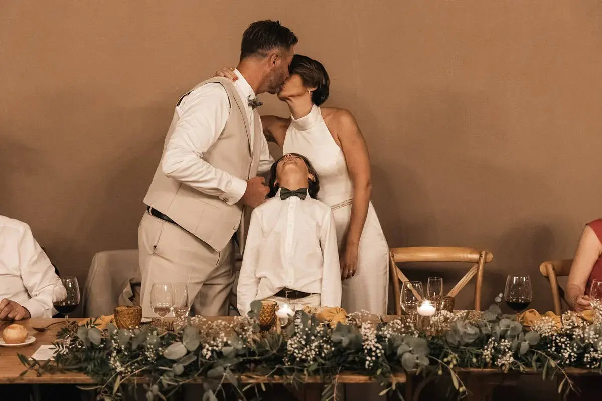 Una pareja se besa tiernamente mientras su hijo mira al cielo, celebrando bodas de plata, oro y platino.