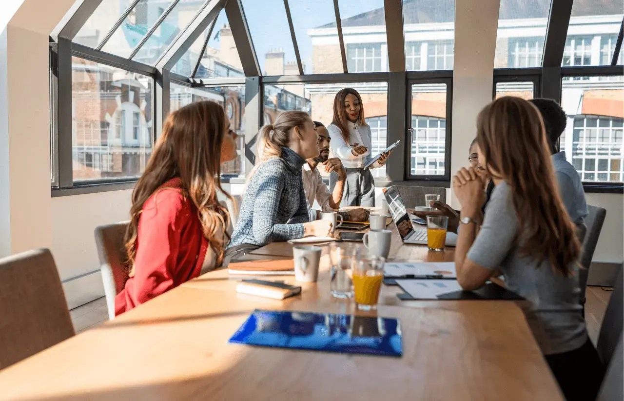 Un grupo diverso de profesionales participa en un workshop, discutiendo ideas alrededor de una mesa con laptops y bebidas.