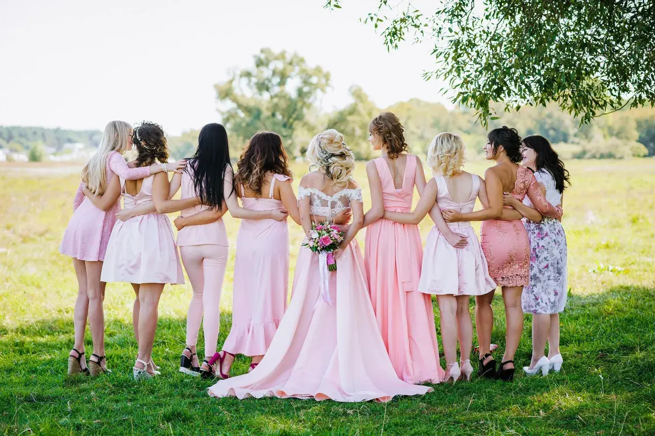 Novia rodeada por sus damas de honor, todas vestidas de rosa, en un campo verde.