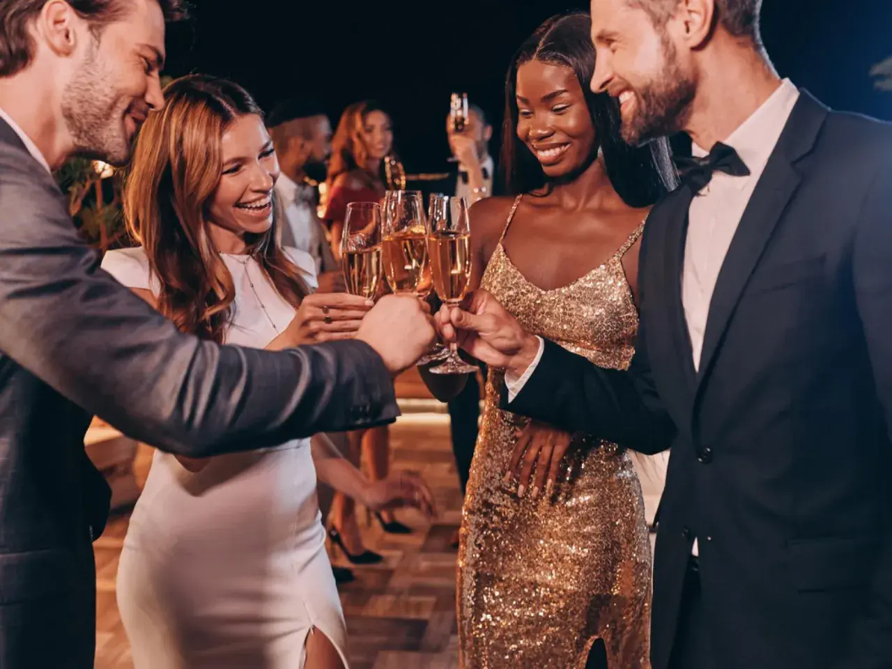 Pareja brinda con champán en una fiesta elegante. Ella luce un vestido dorado brillante, un look perfecto para una **black tie mujer**.