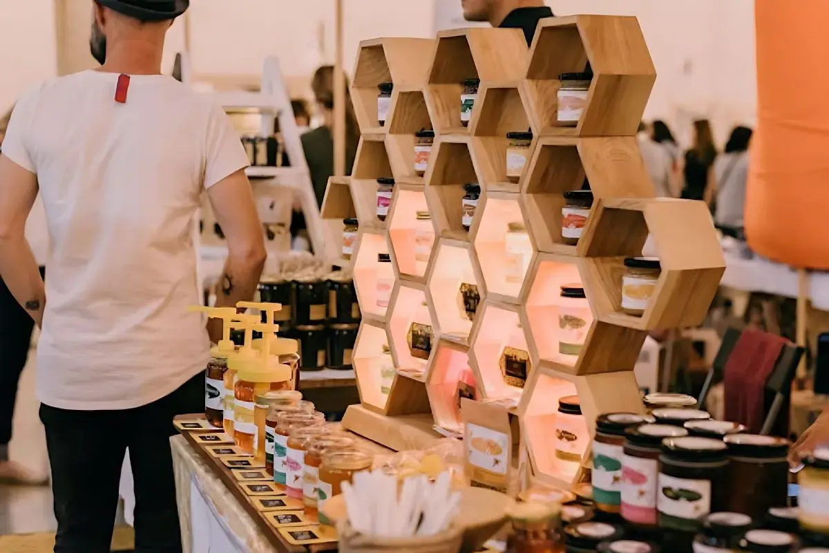 Exhibición de mieles artesanales en ferias empresariales. Tarros de miel en estanterías de madera con forma de panal, iluminados.