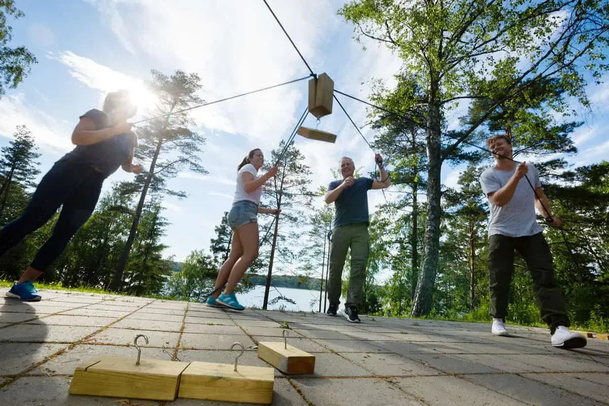 Un grupo participa en un juego de team building outdoor, tirando de cuerdas para mover un objeto de madera.