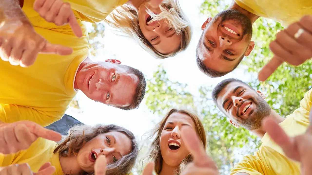 Un grupo de personas sonríe y señala hacia abajo, fomentando el espíritu de equipo. ¡Perfecto para dinamicas de grupo para empresas!
