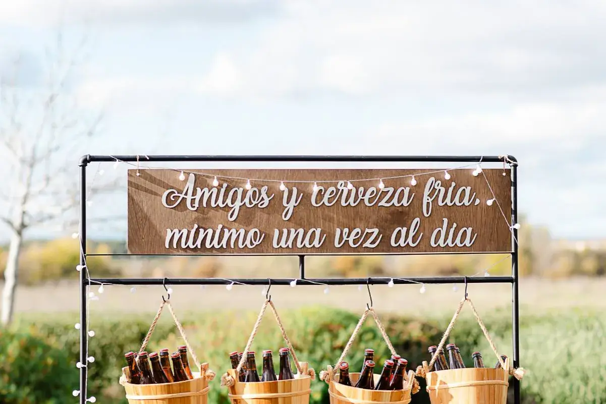 Decoración barra libre boda: letrero "Amigos y cerveza fría, mínimo una vez al día" sobre cubos de cerveza.