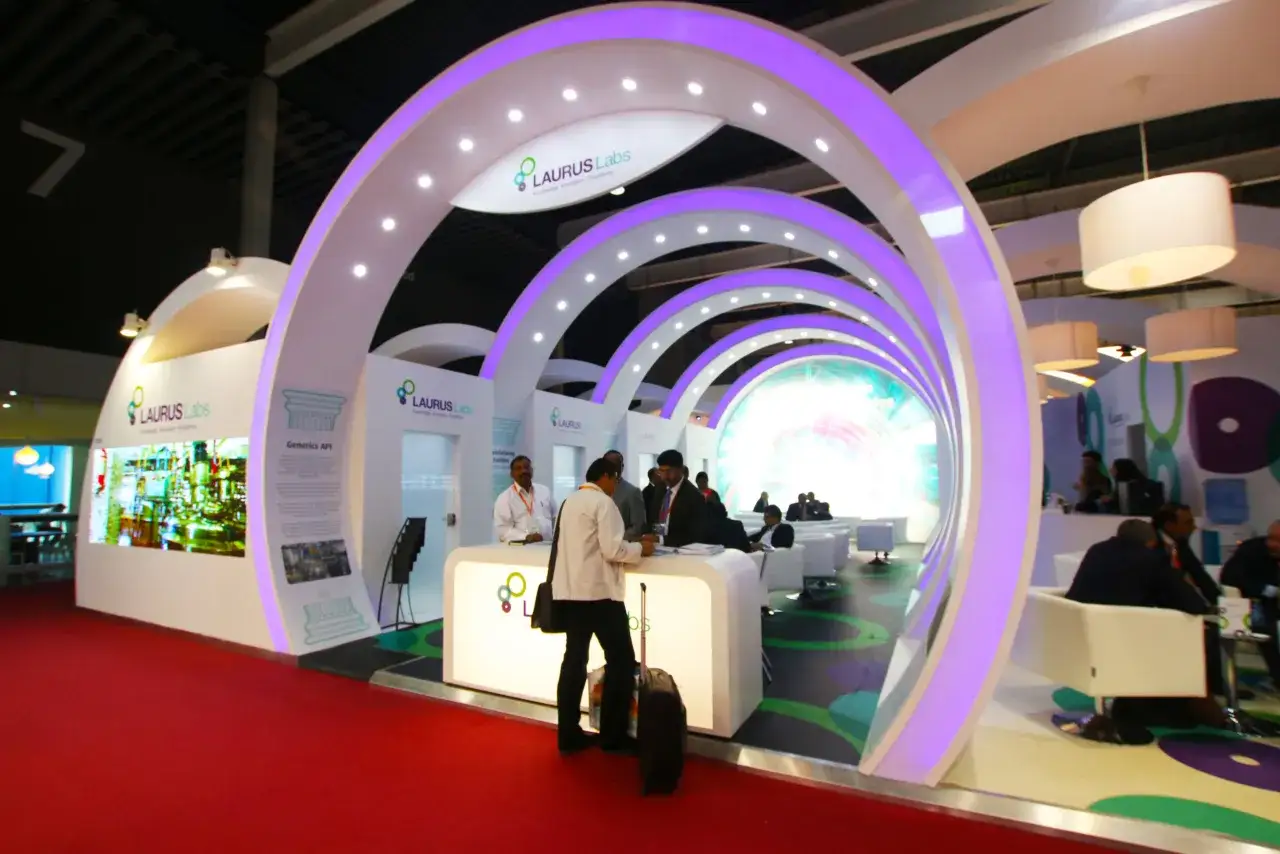 Expositores en un roadshow que es un evento de presentación de Laurus Labs, con un diseño moderno y arcos iluminados en púrpura.