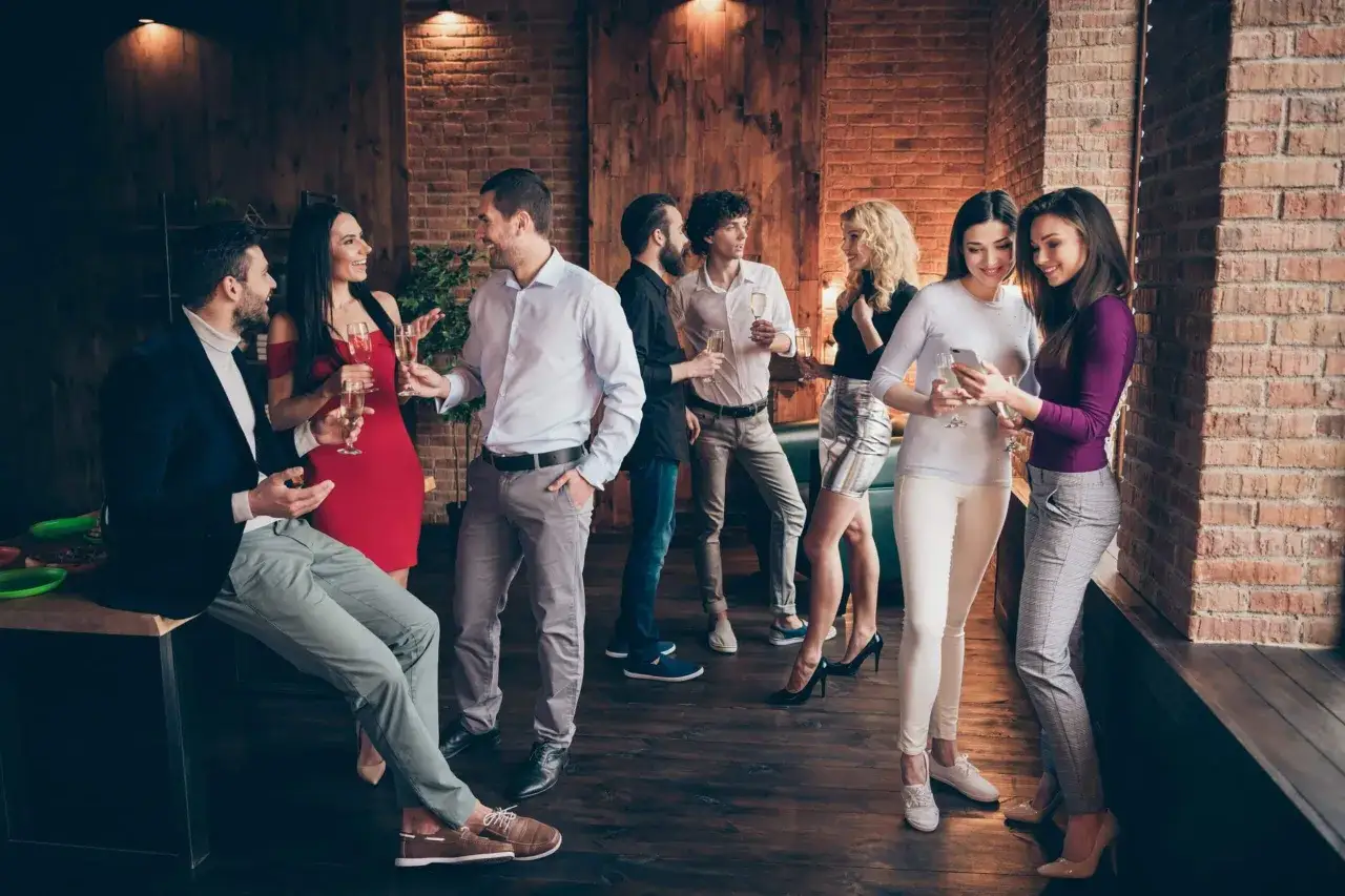 Grupo de amigos disfrutando de una fiesta, todos con un elegante dress code fiesta, brindando con copas de champ&aacute;n en un ambiente moderno.
