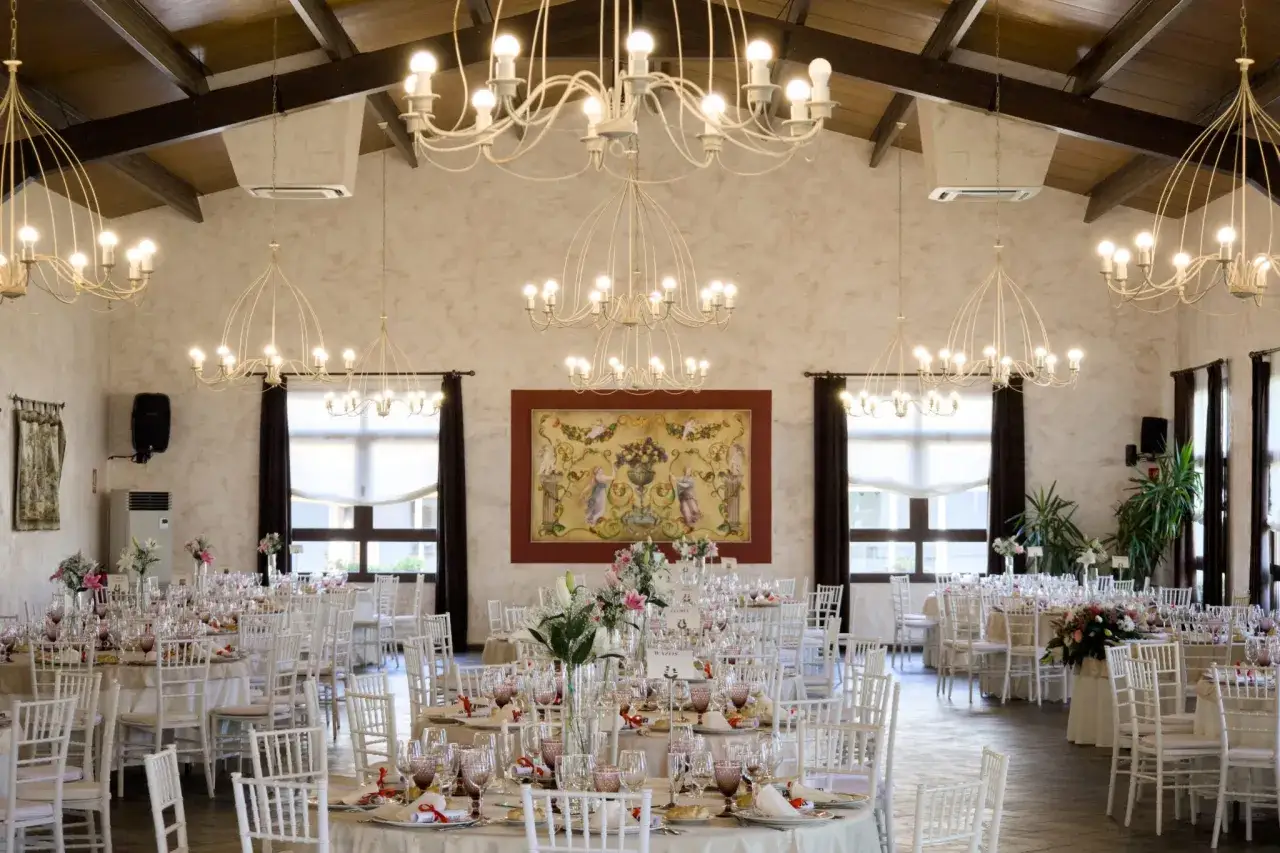 Sal&oacute;n elegante con mesas puestas, perfecto para celebrar las bodas de oro. L&aacute;mparas de ara&ntilde;a y un cuadro central crean un ambiente festivo.