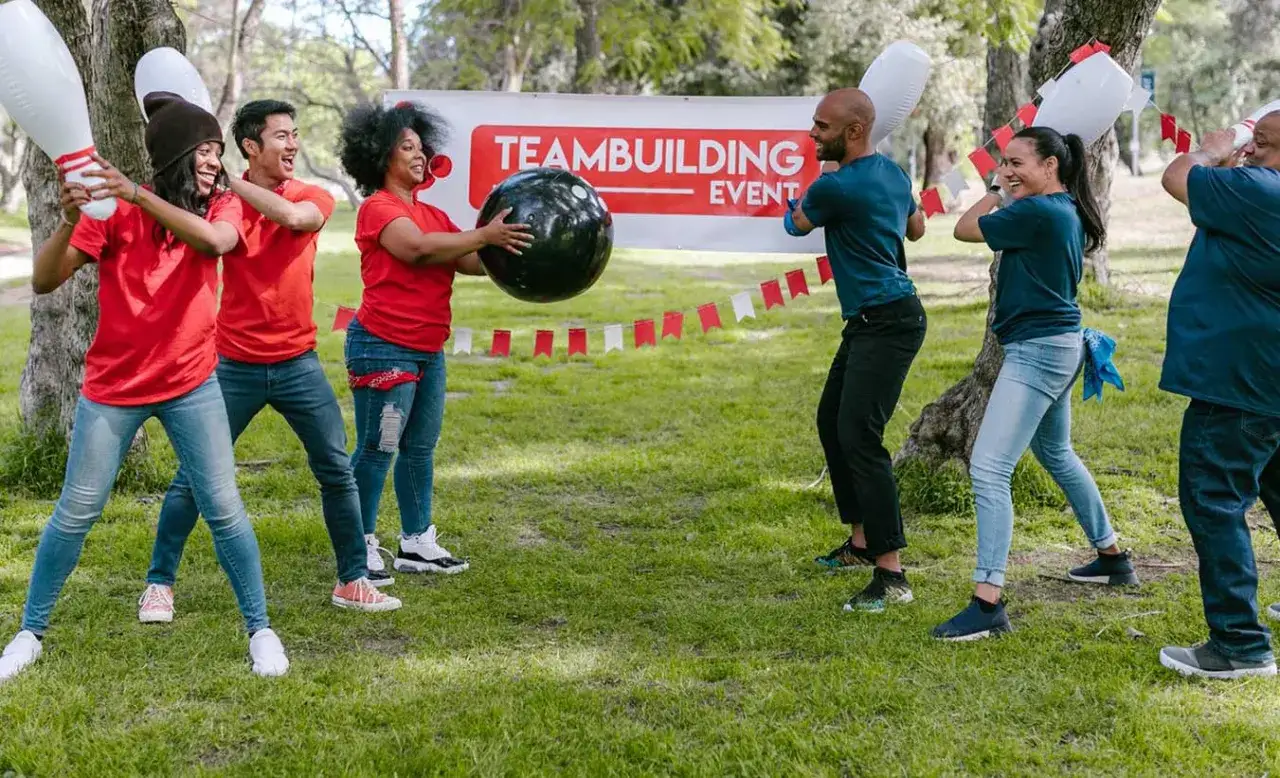 Personas participan en juegos de empresa al aire libre, lanzando una bola gigante y bolos inflables.